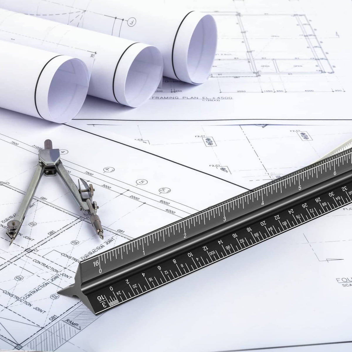Architectural scale ruler on detailed blueprints with rolled plans and drafting tools nearby