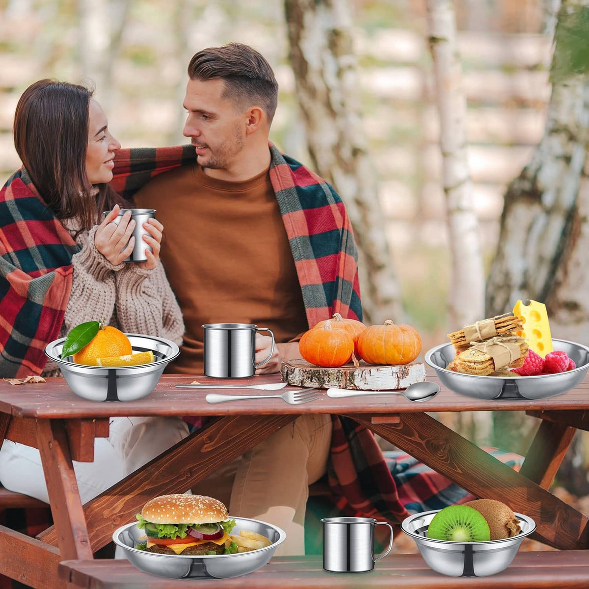 Stainless steel camping cookware set with mugs and bowls on outdoor picnic table