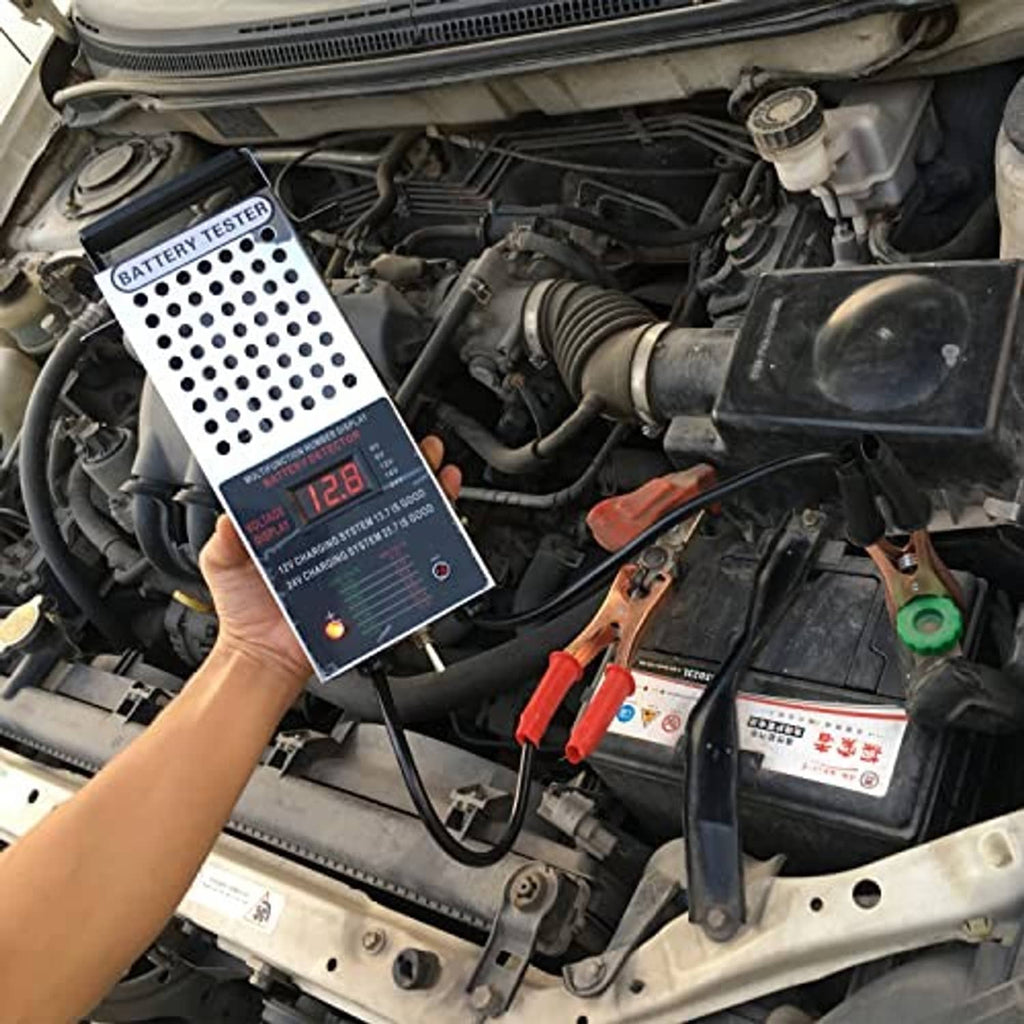 Battery load tester in car engine bay, displaying voltage next to battery clamp cables