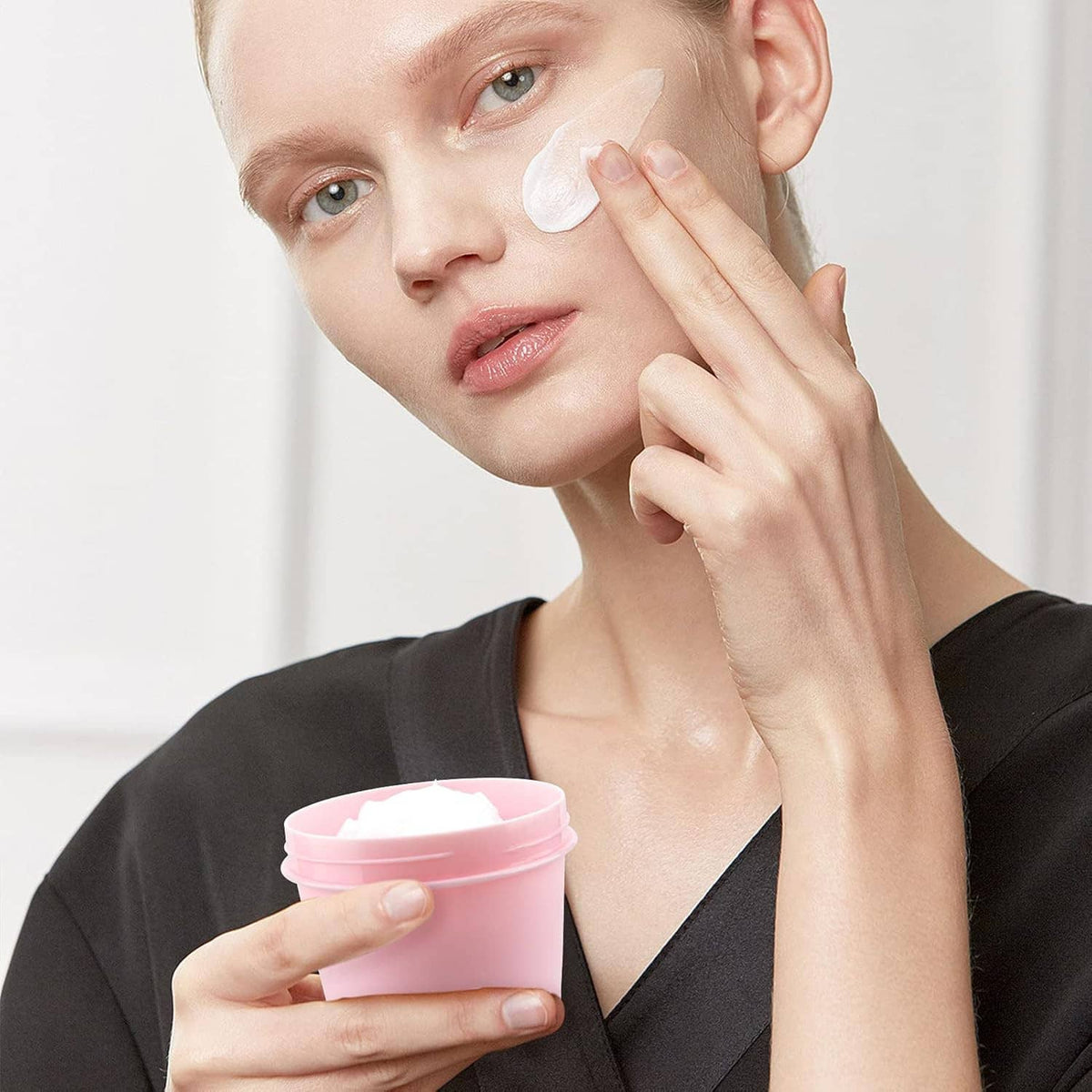 Pink empty plastic cosmetic jar in use, with lid and skincare cream applied