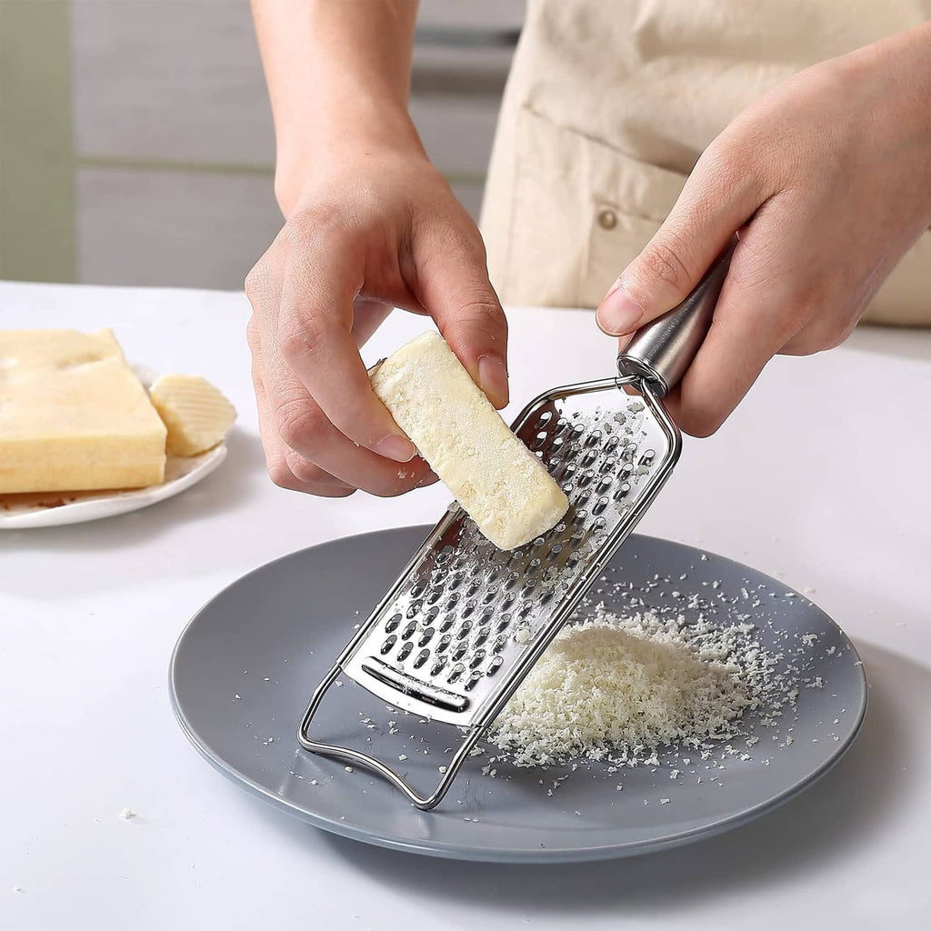 Stainless steel grater being used to grate cheese over a plate