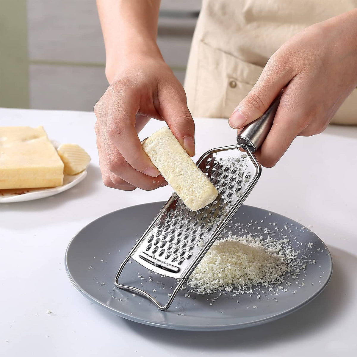 Stainless steel grater being used to grate cheese over a plate