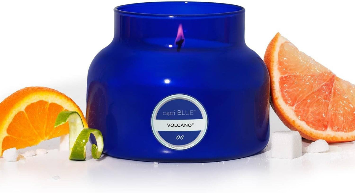 Blue glass jar candle with centered label, flame visible, citrus slices at the sides