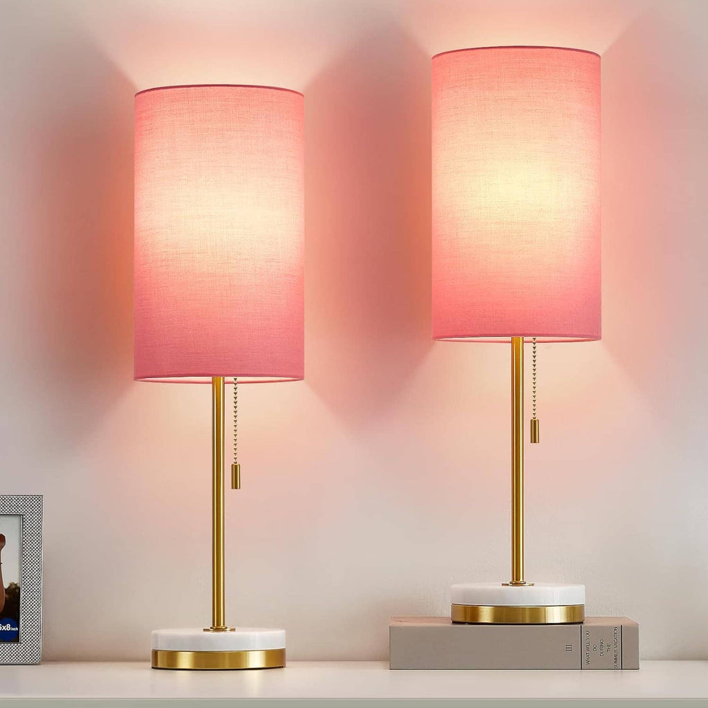 Two minimalist table lamps with pink shades, gold stems, and round white bases facing front.
