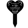 Heart-shaped black remembrance plaque with white verse and floral border on stake.