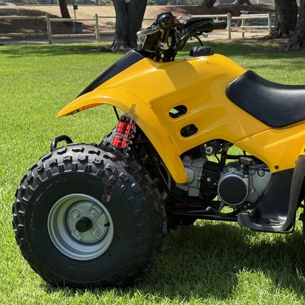 Red front shock absorber on yellow ATV front with black coil spring