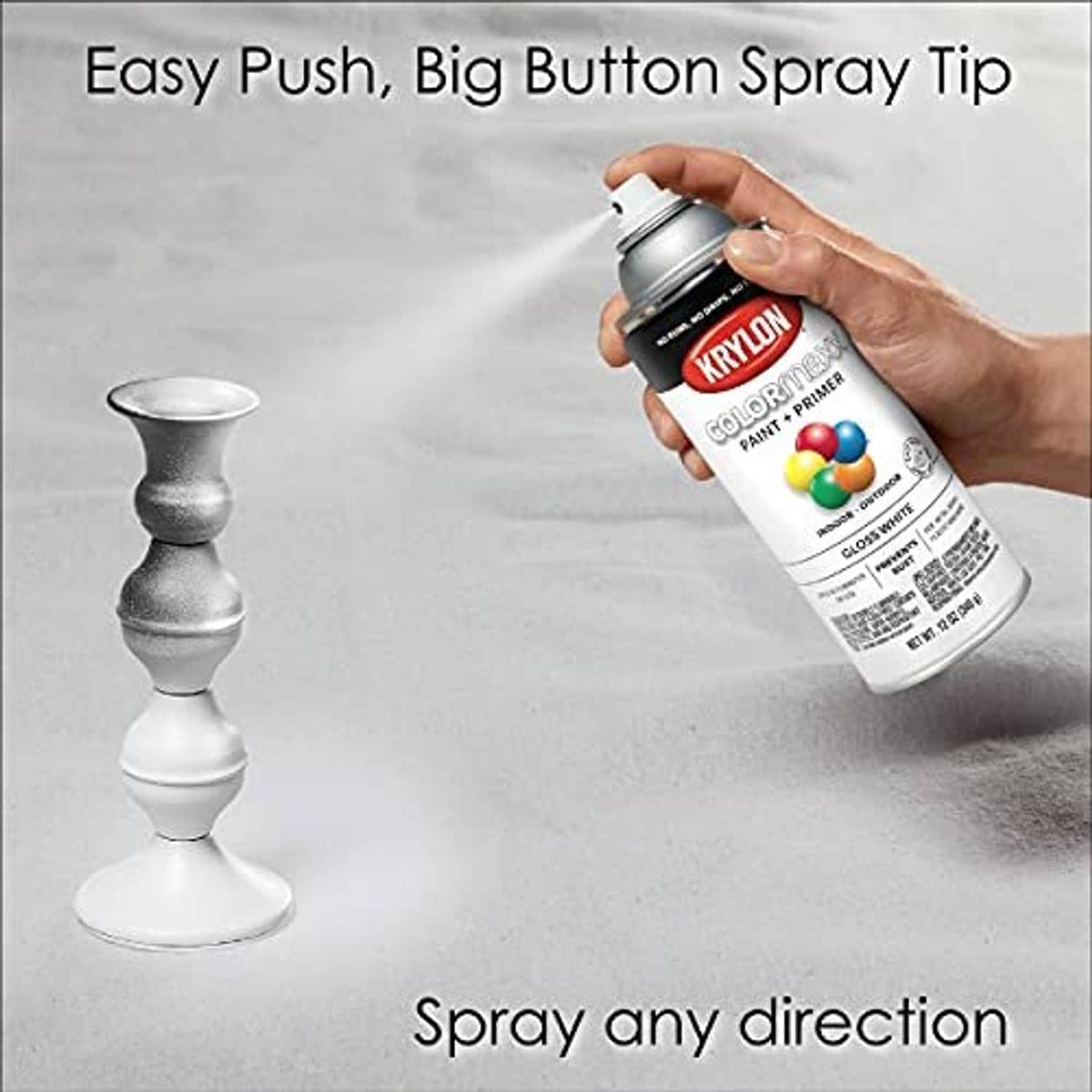 Hand holding spray paint can with adjustable nozzle over a white candlestick