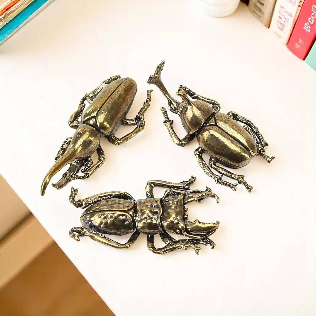 Three brass beetle figurine ornaments arranged on a flat surface