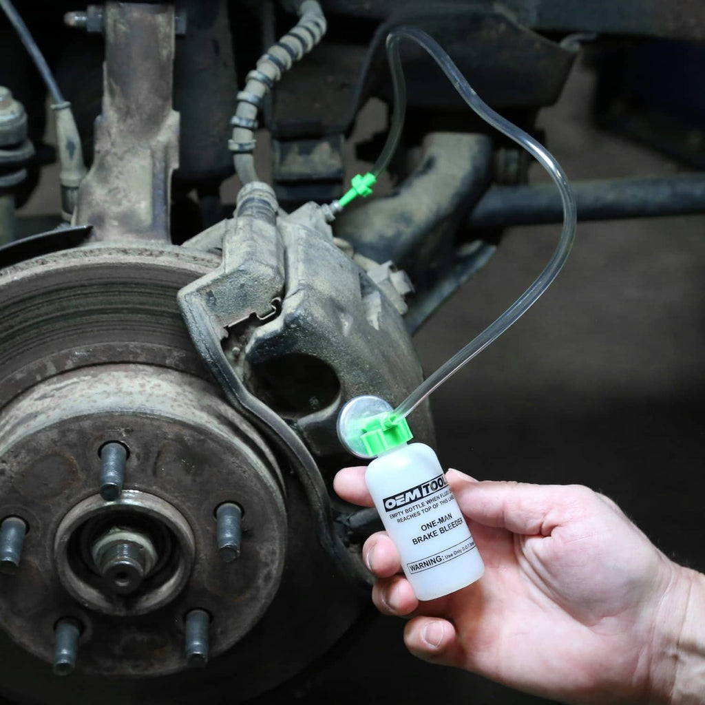 Hand holding brake bleeder bottle near wheel caliper and brake line