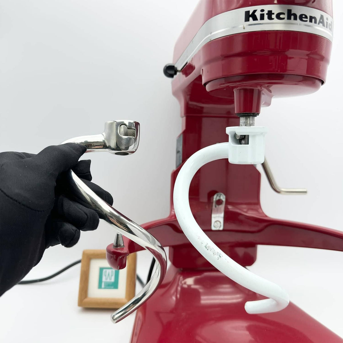 Hand holding stainless steel spiral dough hook near KitchenAid mixer