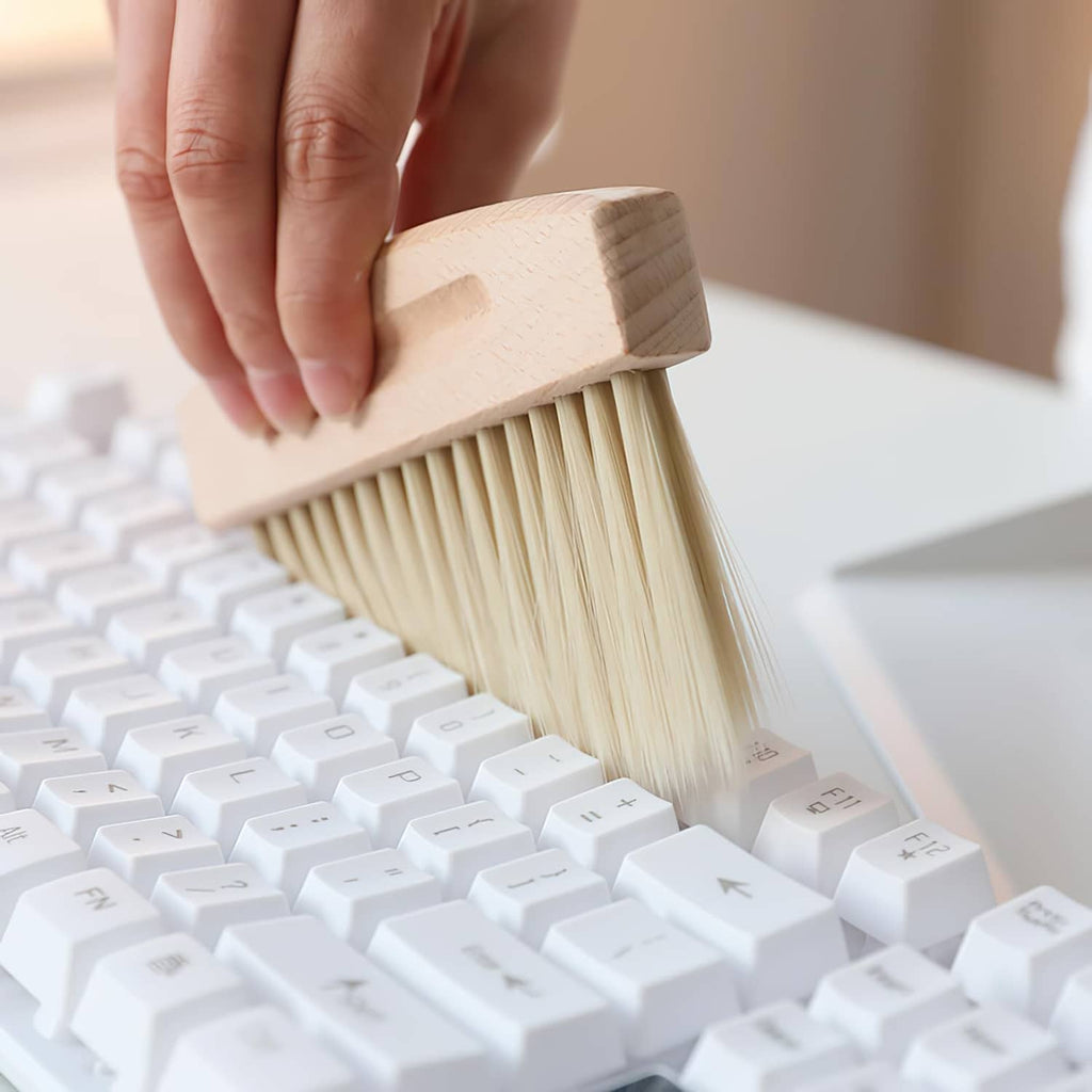 Beige broom brush with beechwood back sweeping small debris near keyboard
