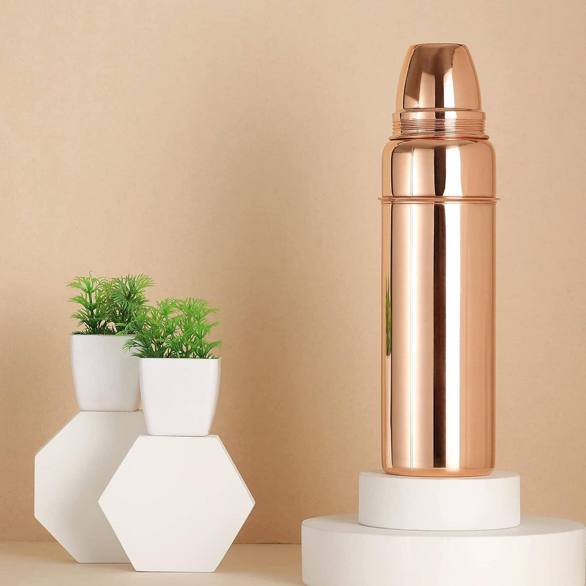 Copper water bottle with screw-on lid on white stand/base