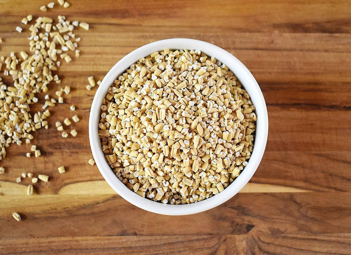 Steel cut oats in a white bowl on a wooden surface, with oats scattered nearby.
