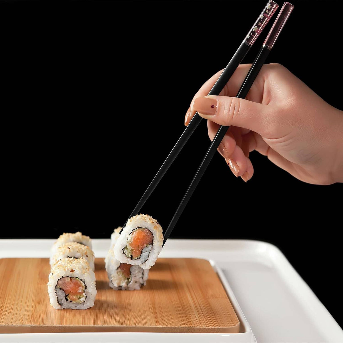 Black reusable chopsticks held in hand picking sushi rolls
