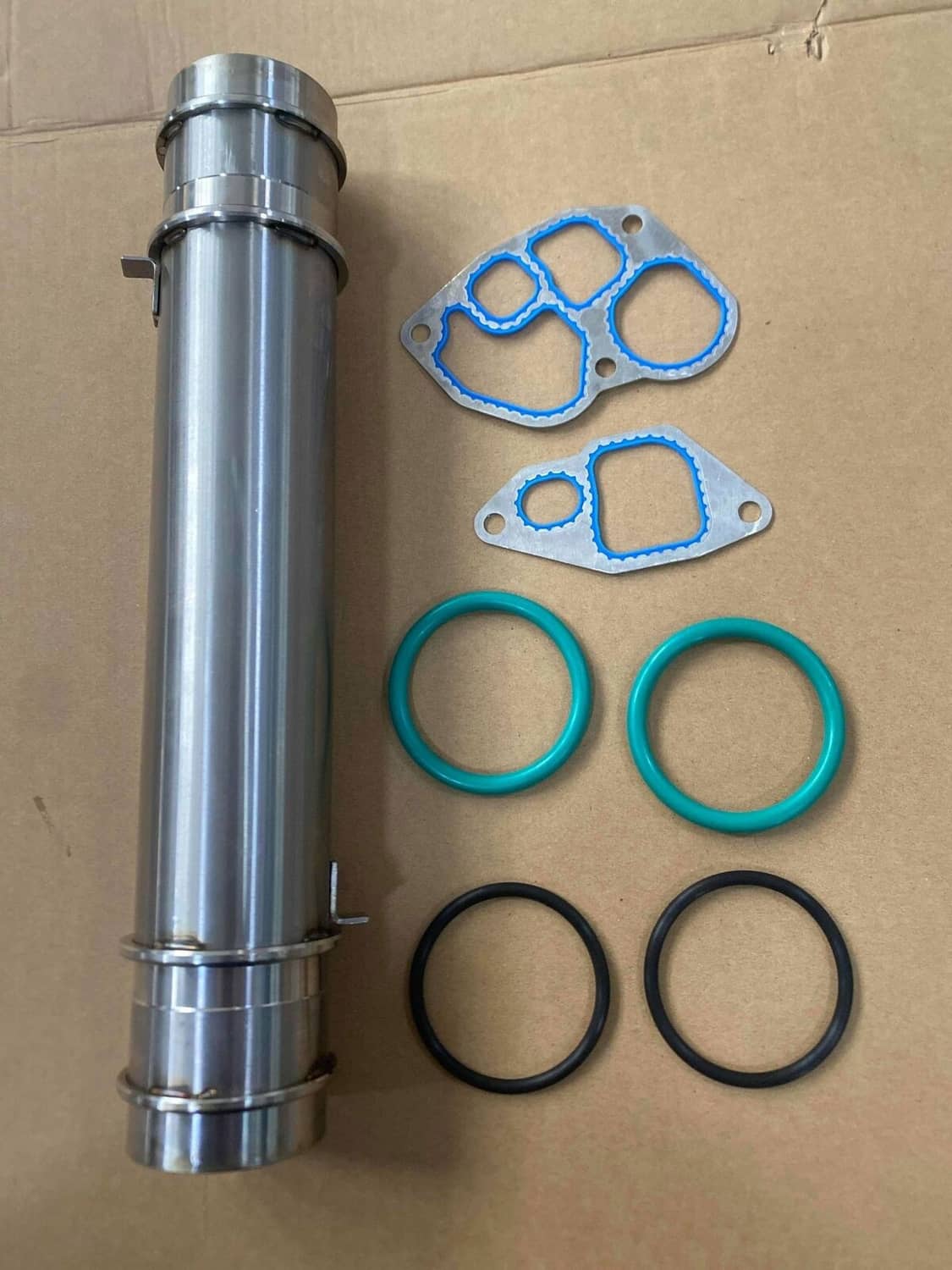 Oil cooler kit on cardboard: silver tube, blue gaskets, and black/green O-rings