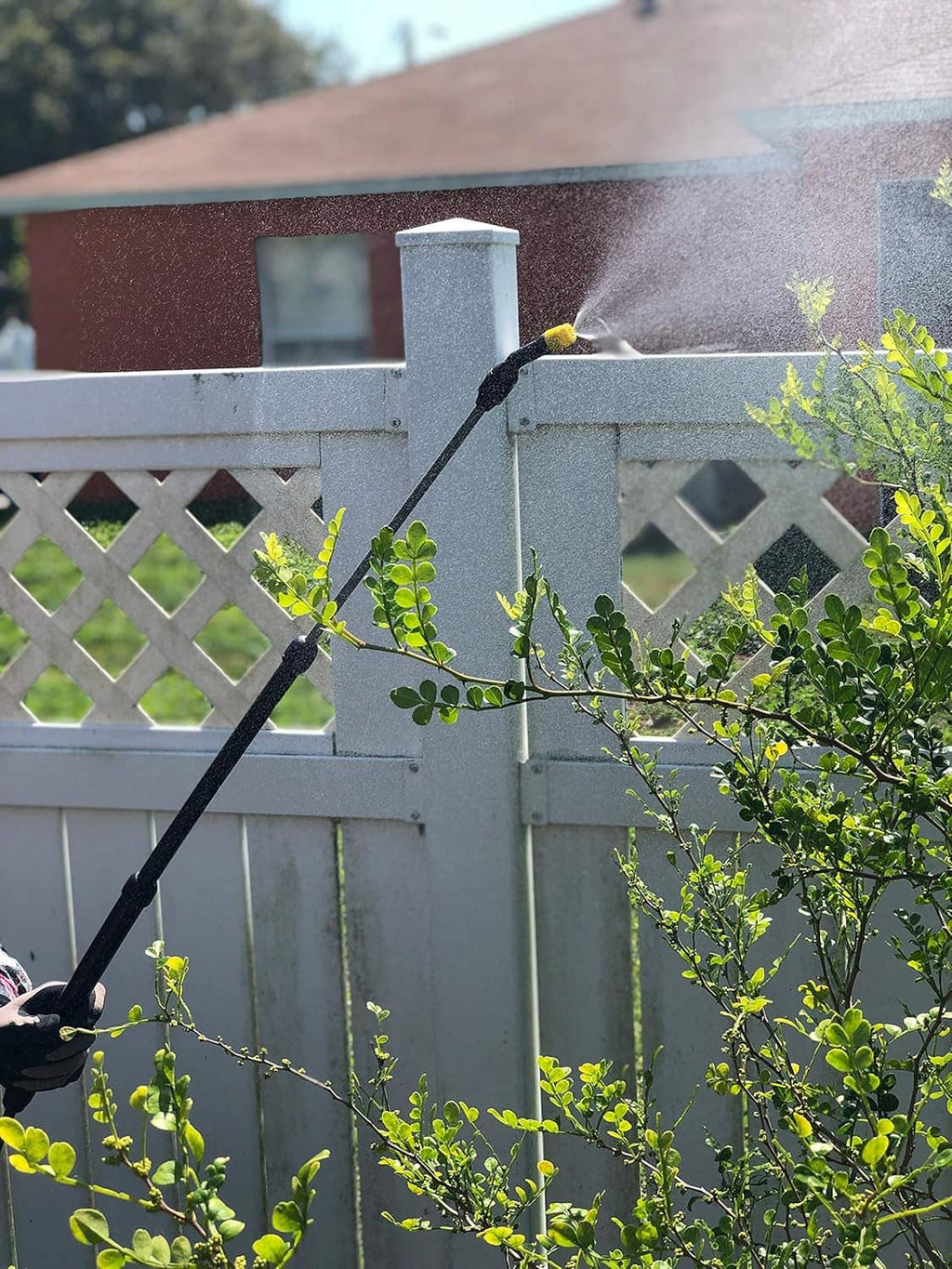 Battery-powered sprayer with black wand spraying from yellow tank near a fence