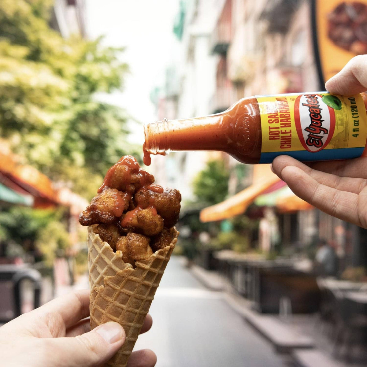 Hand holding El Yucateco red chile habanero hot sauce bottle