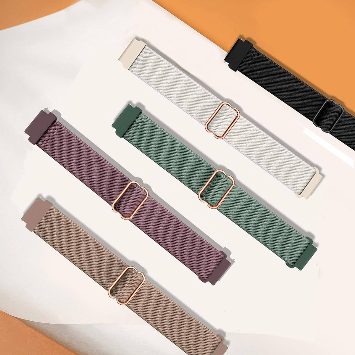 Five watch bands laid out, showing rose-gold metal buckles on fabric loops