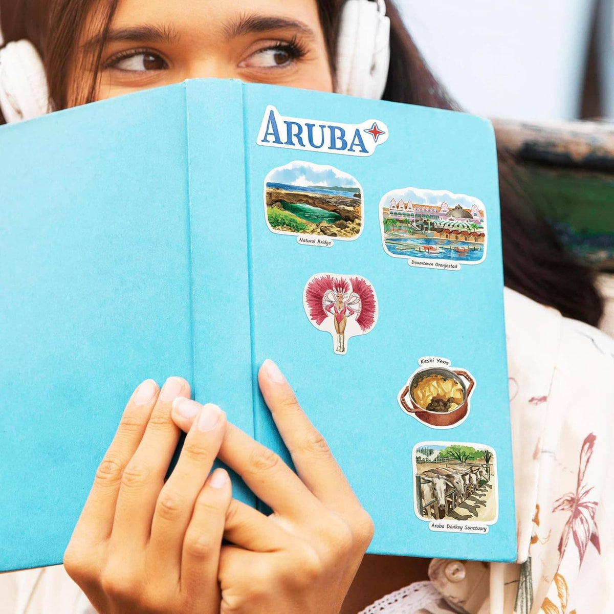 Person holding Aruba travel sticker sheet with beach, flag, and cactus designs