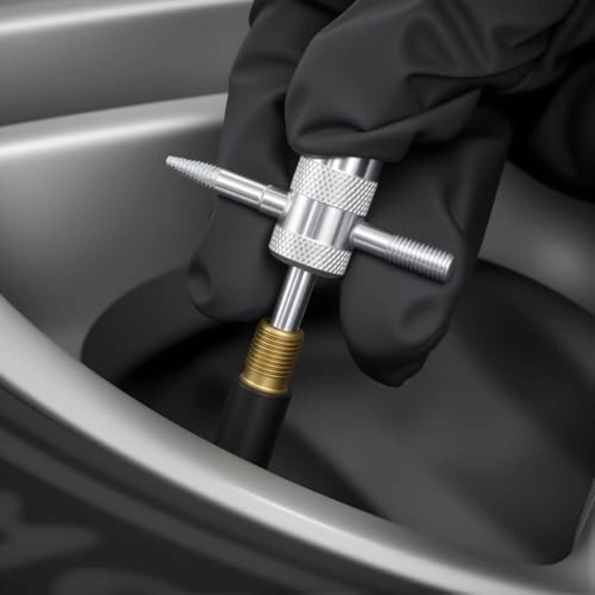 Silver valve core tool held by a gloved hand over a tire valve