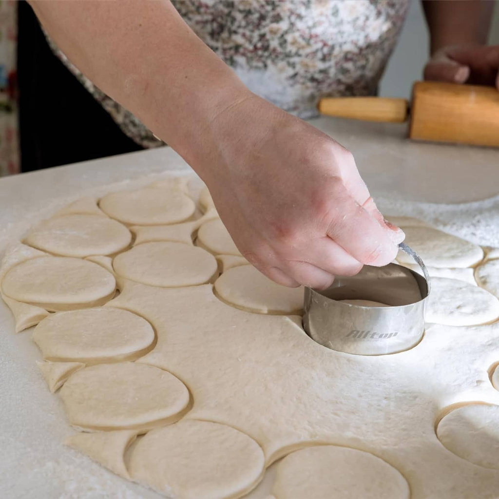 Hand pressing a round stainless steel biscuit cutter into dough