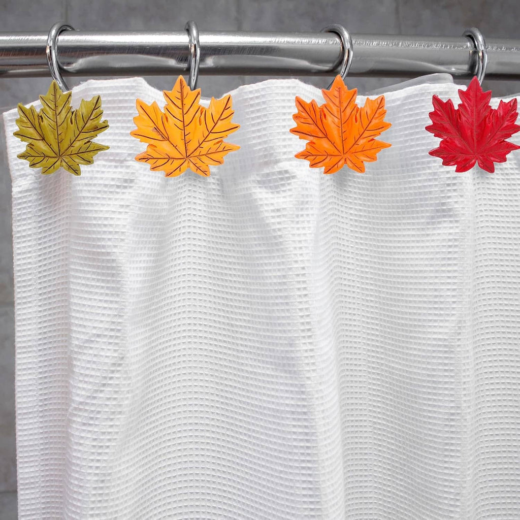 White shower curtain with leaf-shaped shower curtain hooks; chrome rings with multicolor leaves