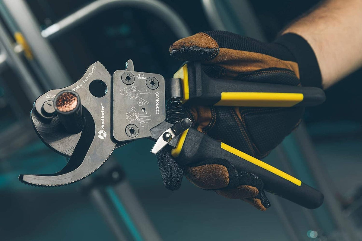 Ratcheting cable cutter tool held in gloved hand with yellow and black grips