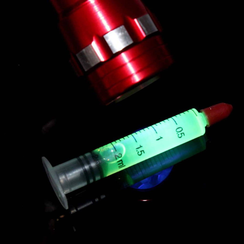 Green measurement syringe with plunger beside glowing UV light for leak detection
