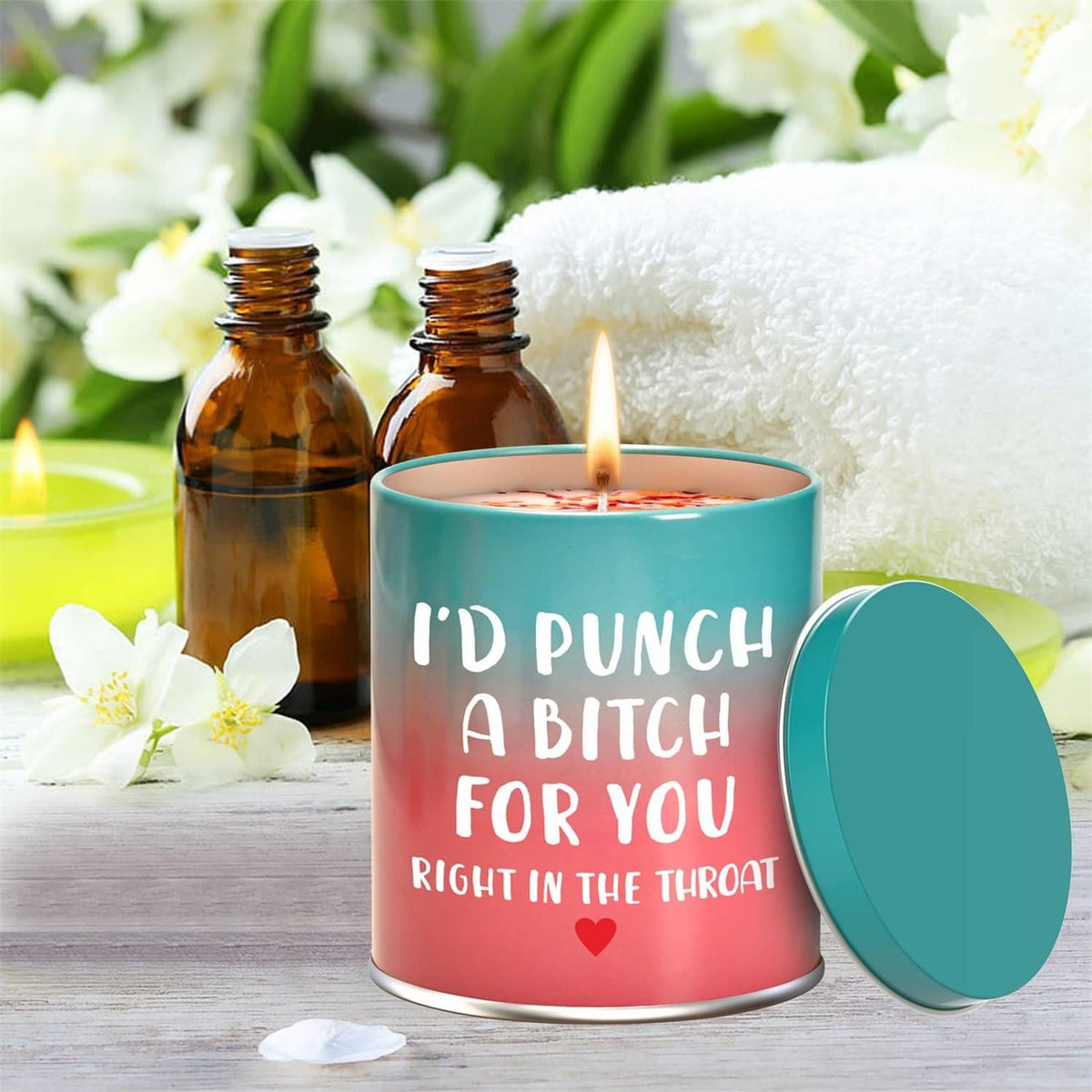 Scented candle in teal and pink metal cup with lid, near amber oil bottles