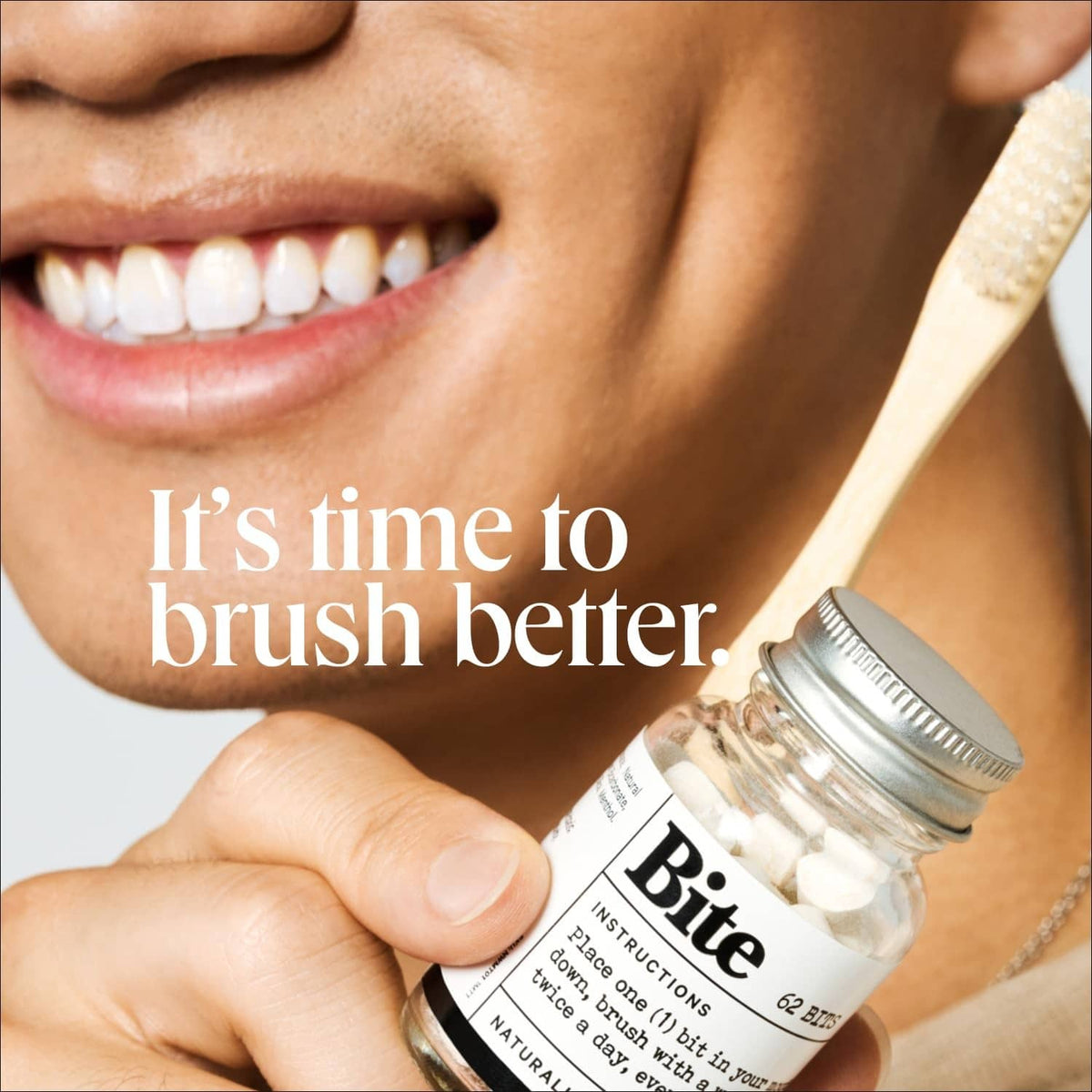Hand holding a Bite toothpaste tablets jar with wooden brush and bright smile