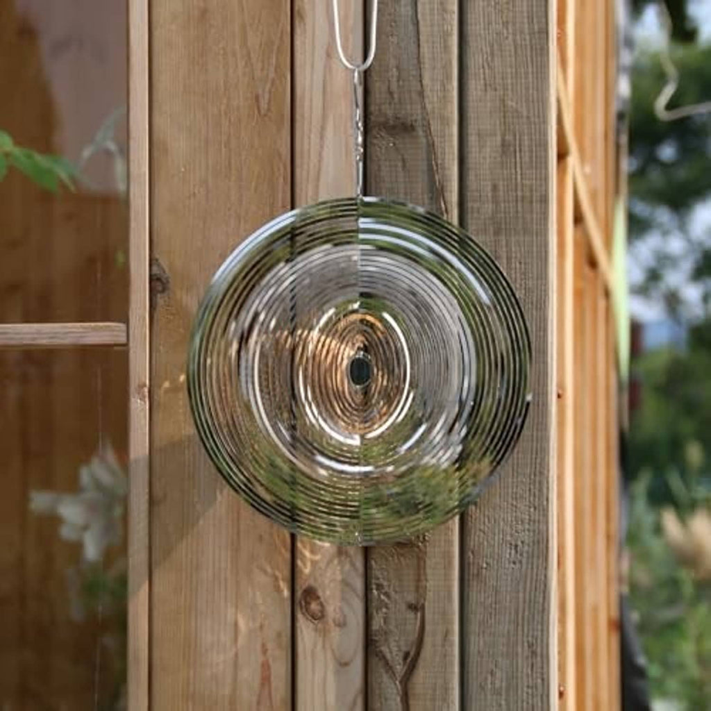 Silver round wind spinner hanging from a wooden fence with concentric metal rings