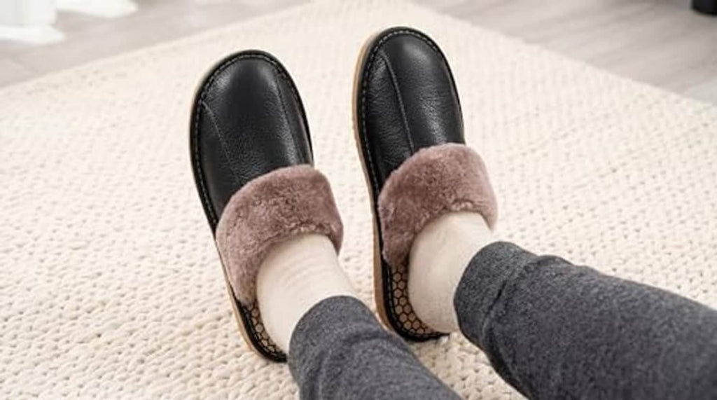 Pair of unisex black leather slippers with plush taupe lining on feet with socks.