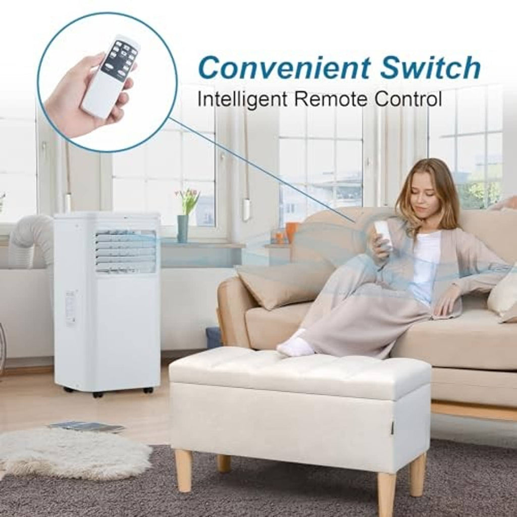 White portable air conditioner beside sofa, with remote control held in hand
