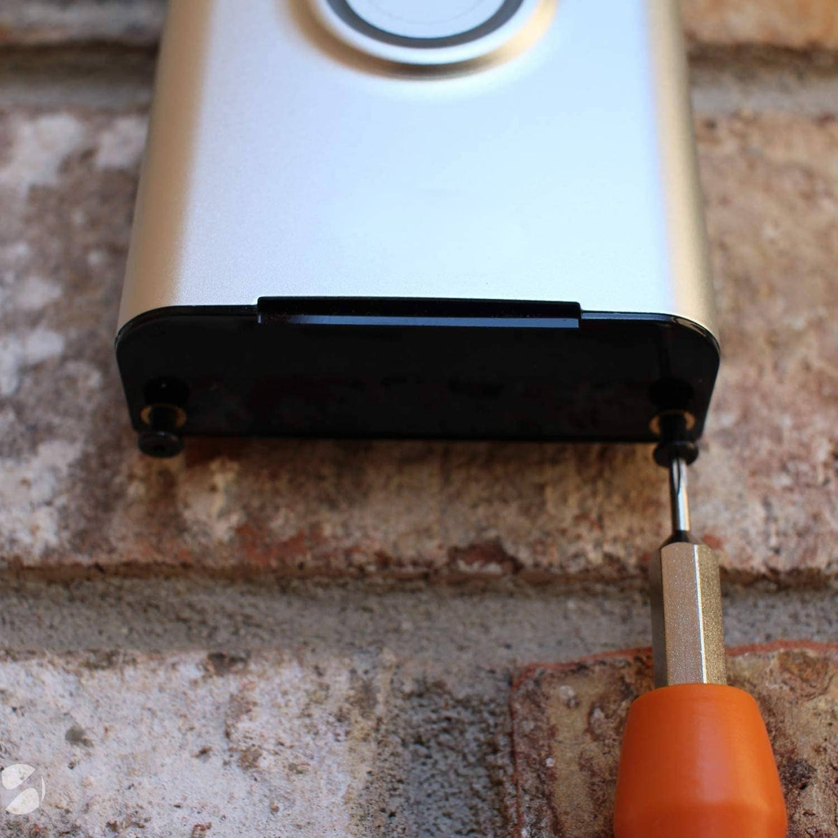Orange-handled screwdriver using steel bit at a doorbell mounting screw on exterior wall