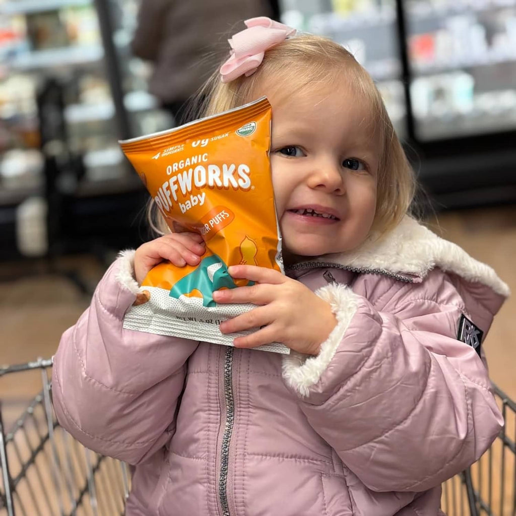 Toddler holding an orange Puffworks baby peanut butter puffs pouch