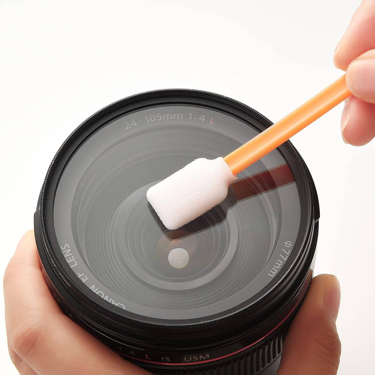 Hand holding an orange foam swab; white foam tip cleaning a camera lens.