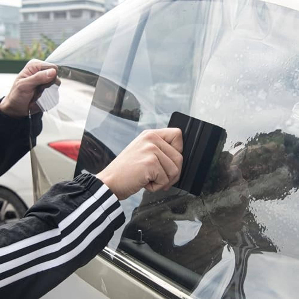 Black vinyl wrap squeegee smoothing film on a car window