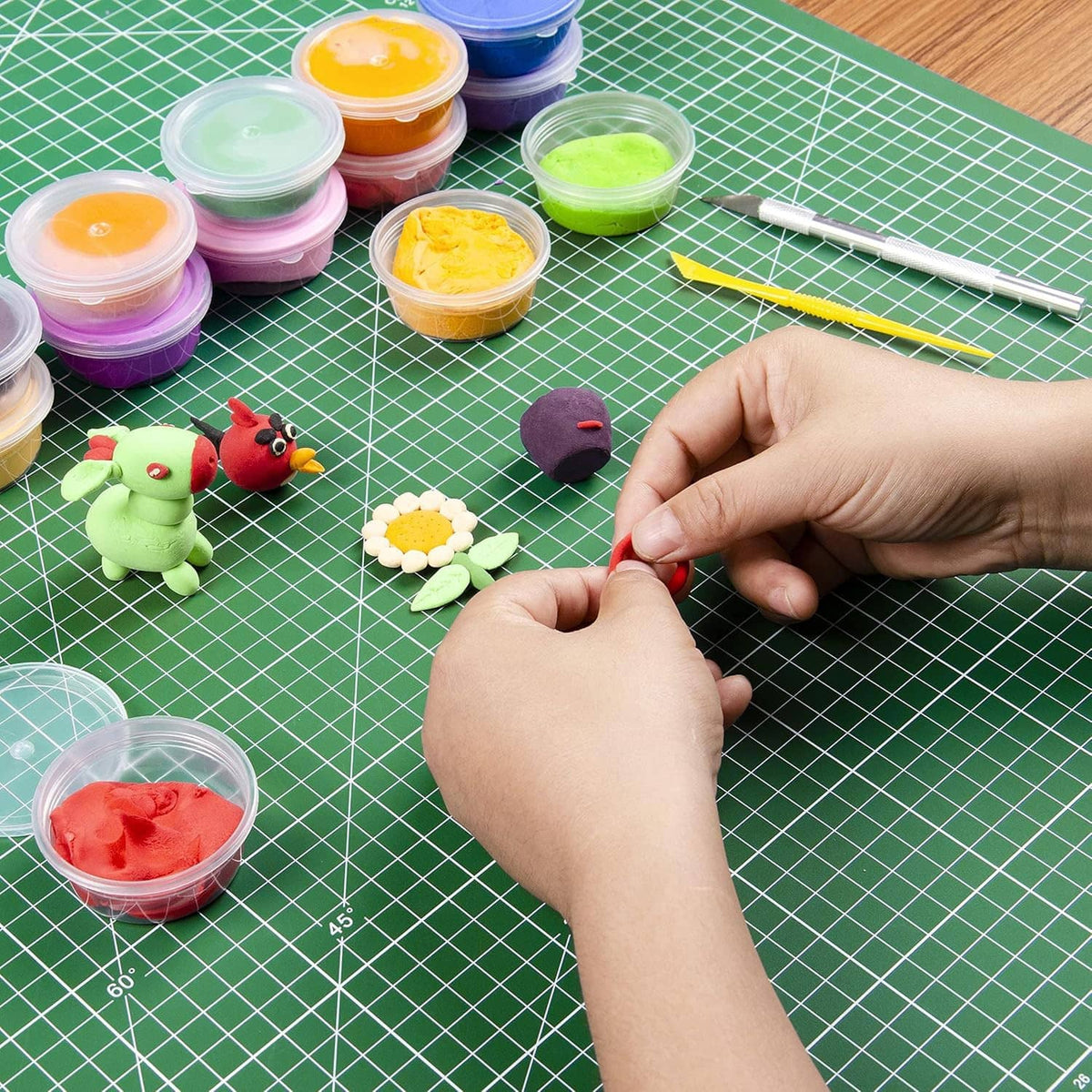 Green gridded cutting mat with hands crafting small pieces and paint containers nearby