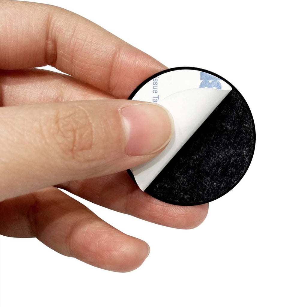 Hand peels backing from black adhesive metal plate disk, exposing sticky adhesive