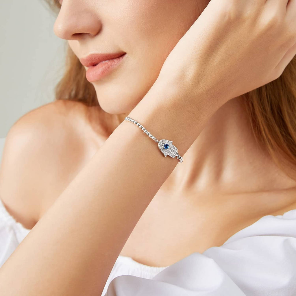 Silver hamsa bracelet worn on wrist with blue center charm and beaded links