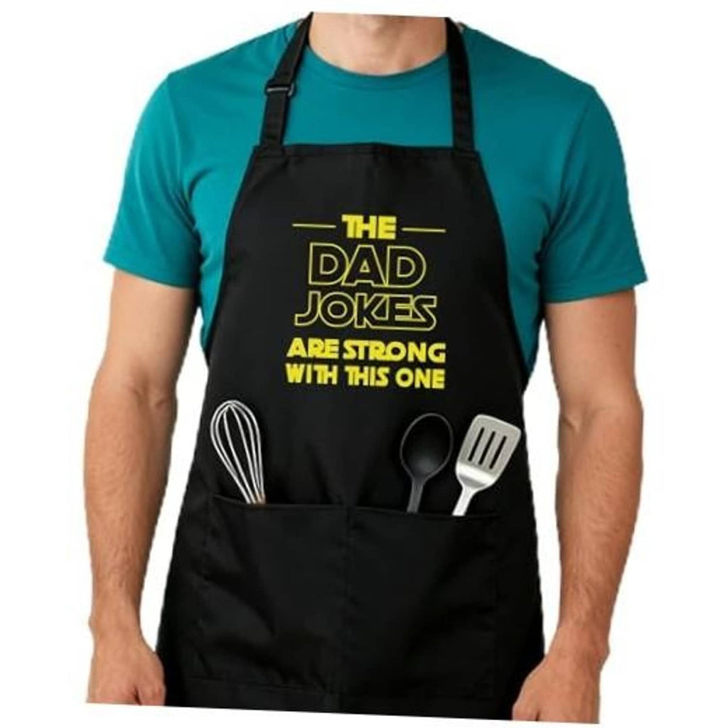 Black cooking apron on teal shirt with adjustable straps and utensil graphic