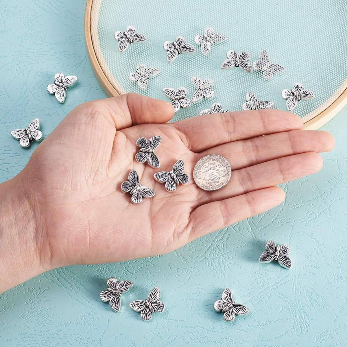 Antique silver butterfly spacer beads in hand, with small coin for scale