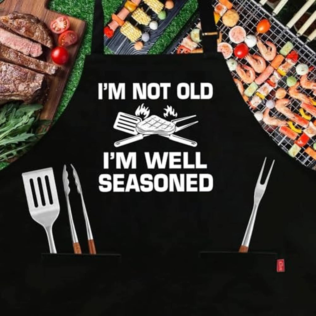 Black BBQ apron with “I’M NOT OLD, I’M WELL SEASONED” text and grill utensil icon