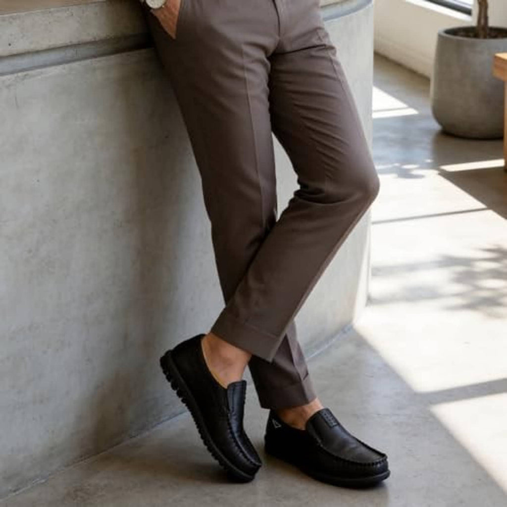 Black slip-on loafers worn with brown pants; stitched moc-toe and textured sole