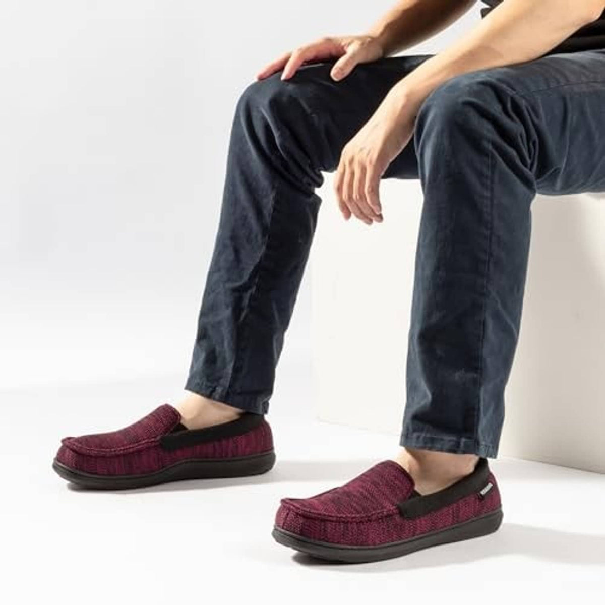 Men's burgundy tweed moc slippers worn with dark jeans, slip-on style