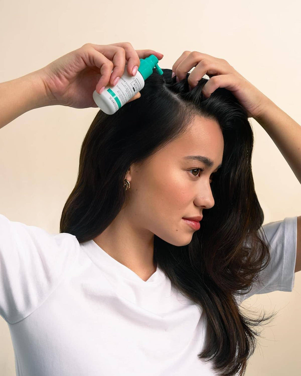 Woman applying teal-tipped scalp serum onto her hair part with both hands