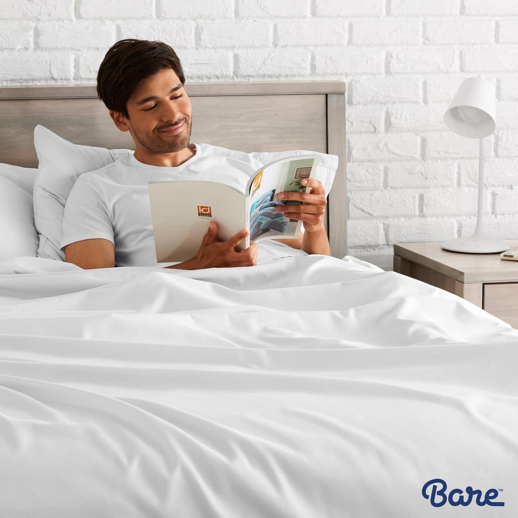 White flat sheet set on a bed as a person reads in a bedroom