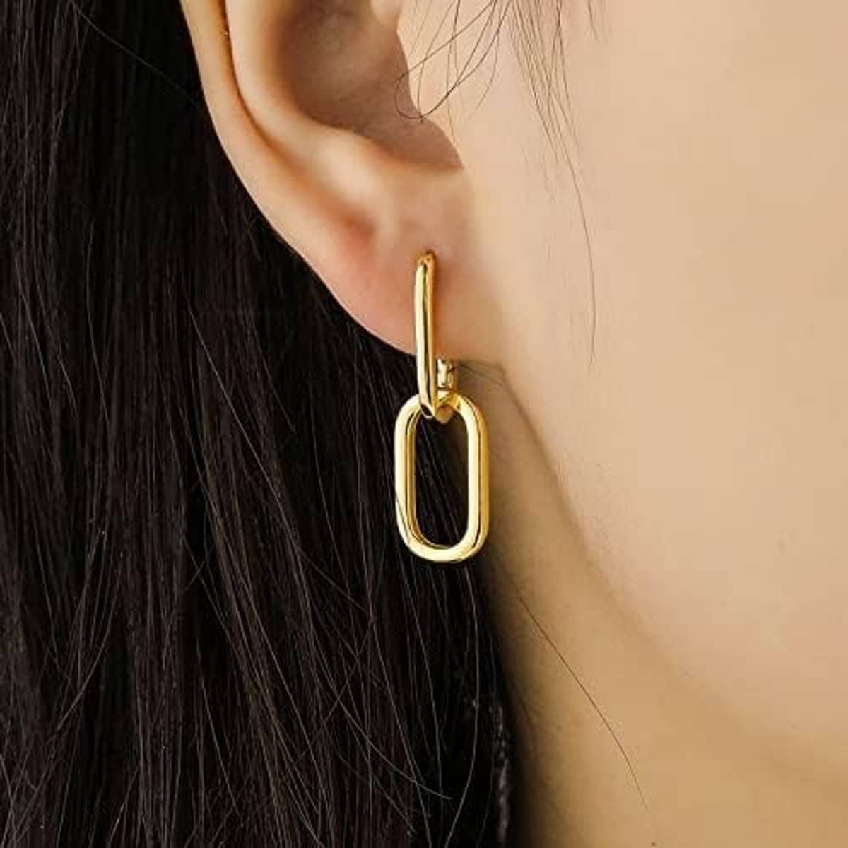 Gold rectangular hoop huggie earring with polished finish on ear