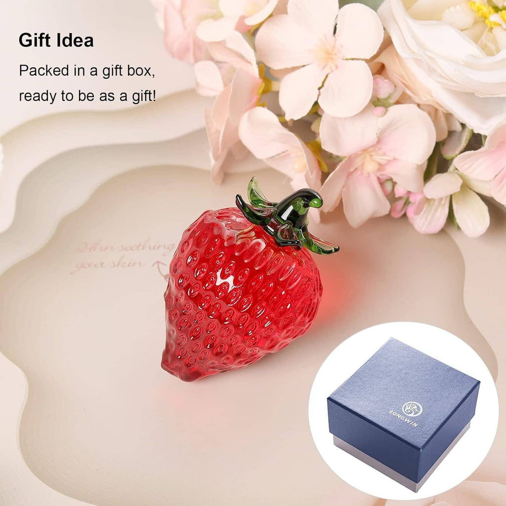 Red glass strawberry paperweight figurine with green leaves beside gift box