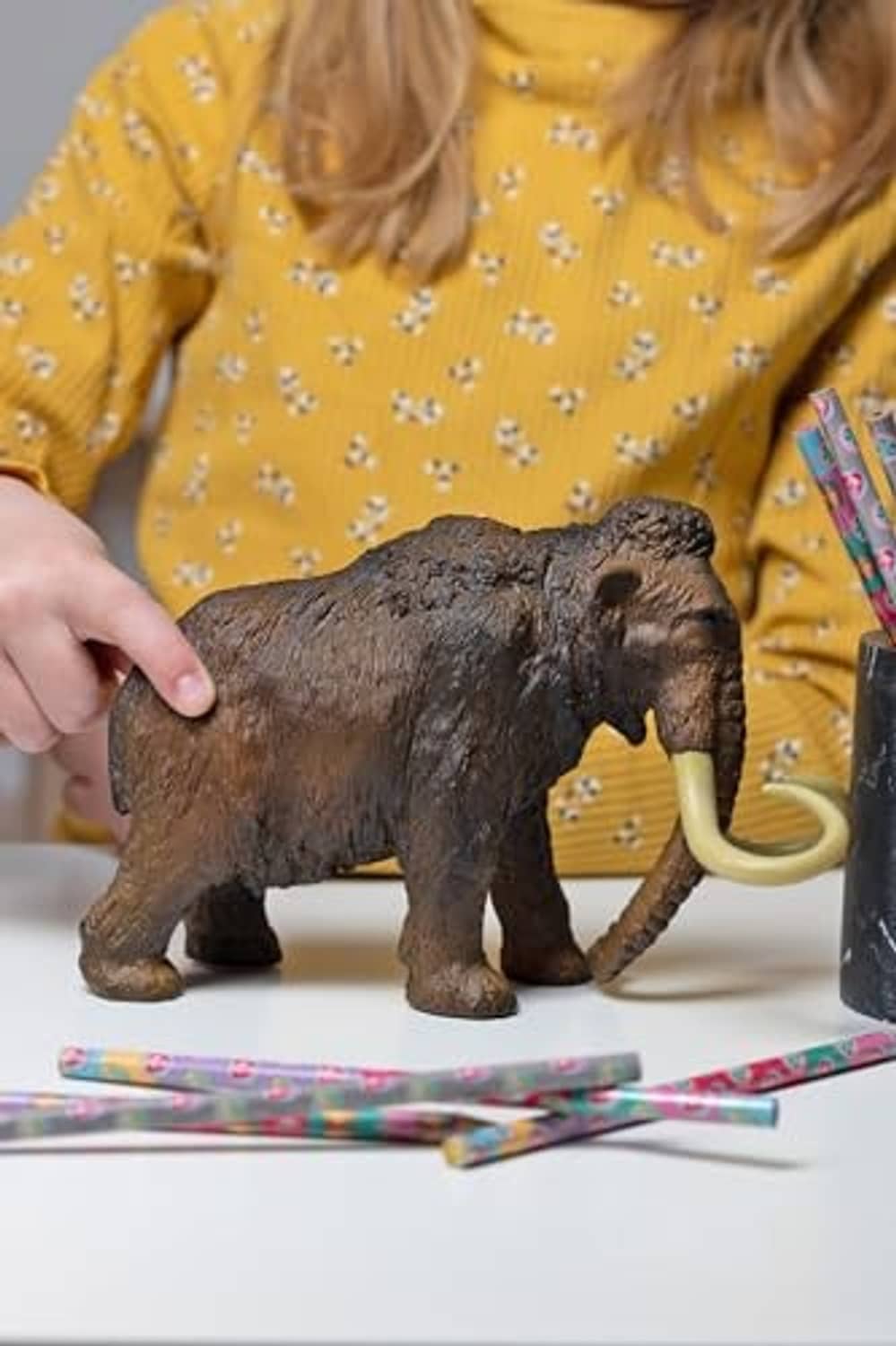 Woolly mammoth toy with long ivory tusks on tabletop, side view